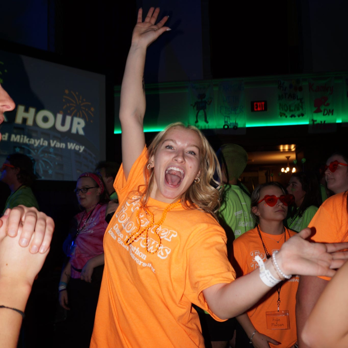 Student in orange shirt jumping in the air at the Big Event