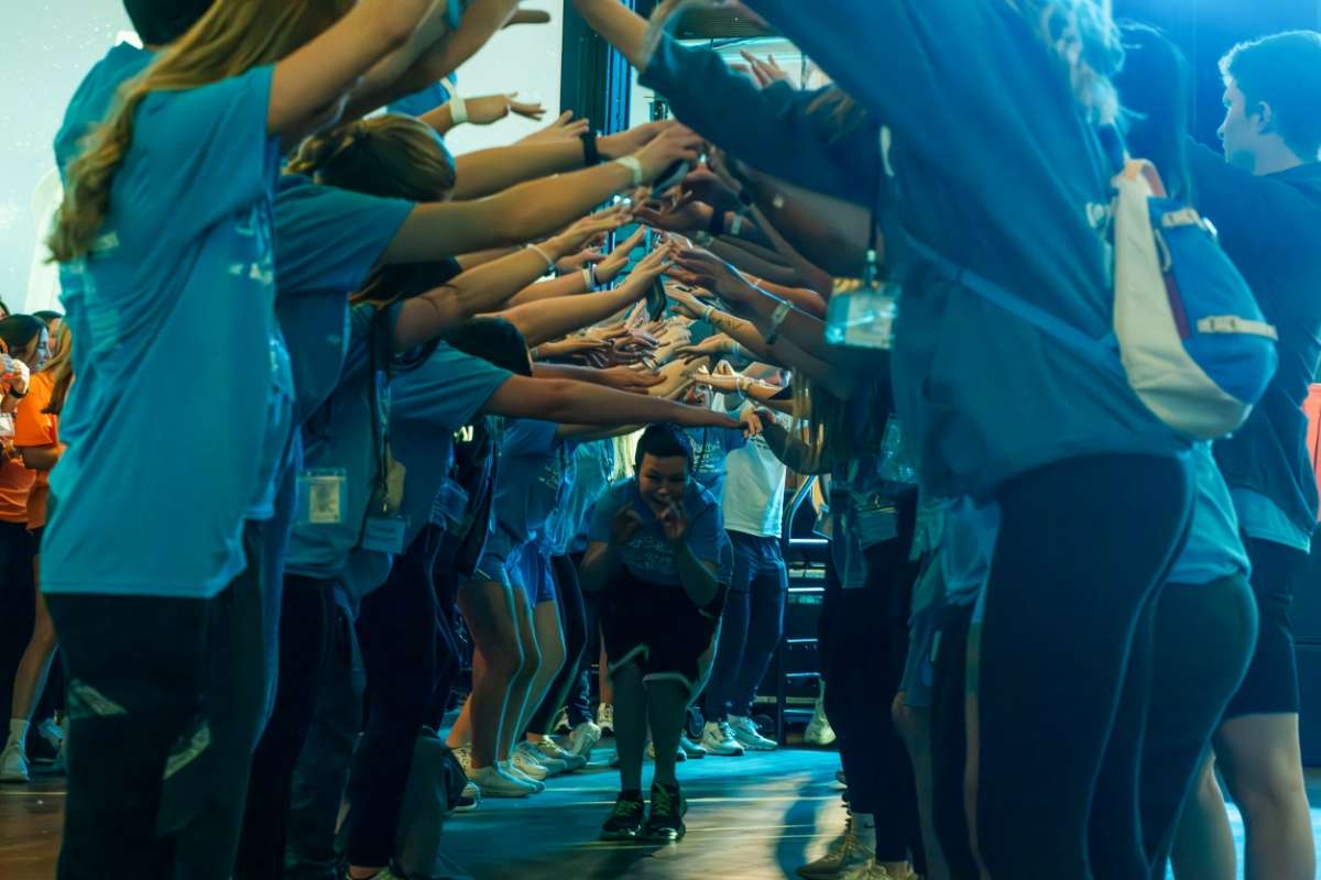 Students in blue tshirts with arms up to form a tunnel that miracle kid is running through